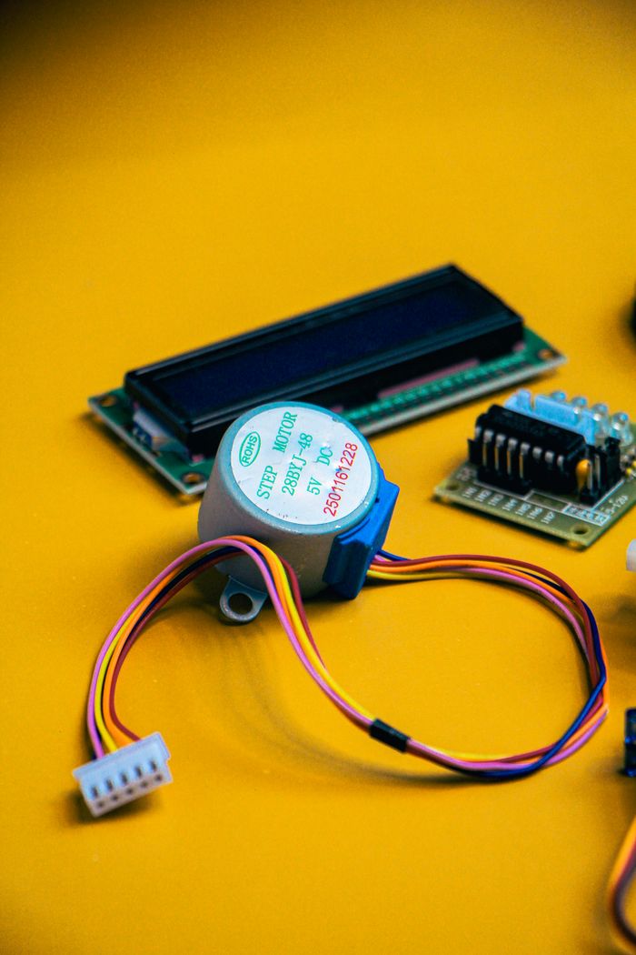 Close-up of electronic components including a step motor and circuit board on a vibrant yellow background.